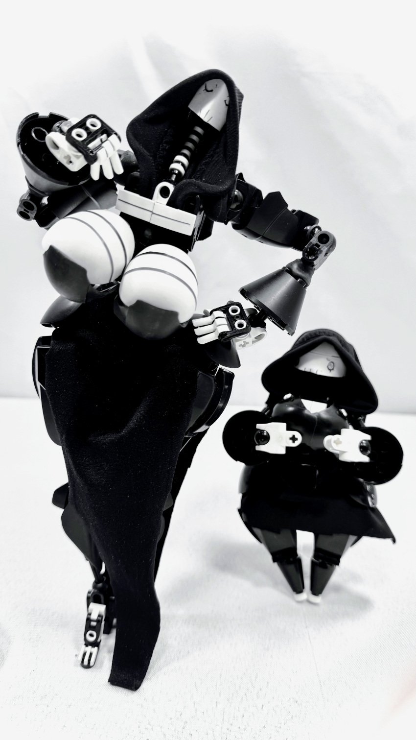 2girls bionicle black_dress black_hoodie dawnofnssd dinner_(dawnofnssd) domna_echelle_(dawnofnssd) edited grim_reaper large_breasts lego size_difference